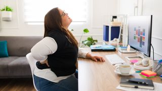 Woman sitting at desk holds her lower back and winces in pain