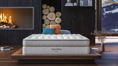 Best king size mattresses: image shows the Saatva Classic hybrid mattress placed on a stylish dark wood bedframe placed in front of a log fire in a cabin