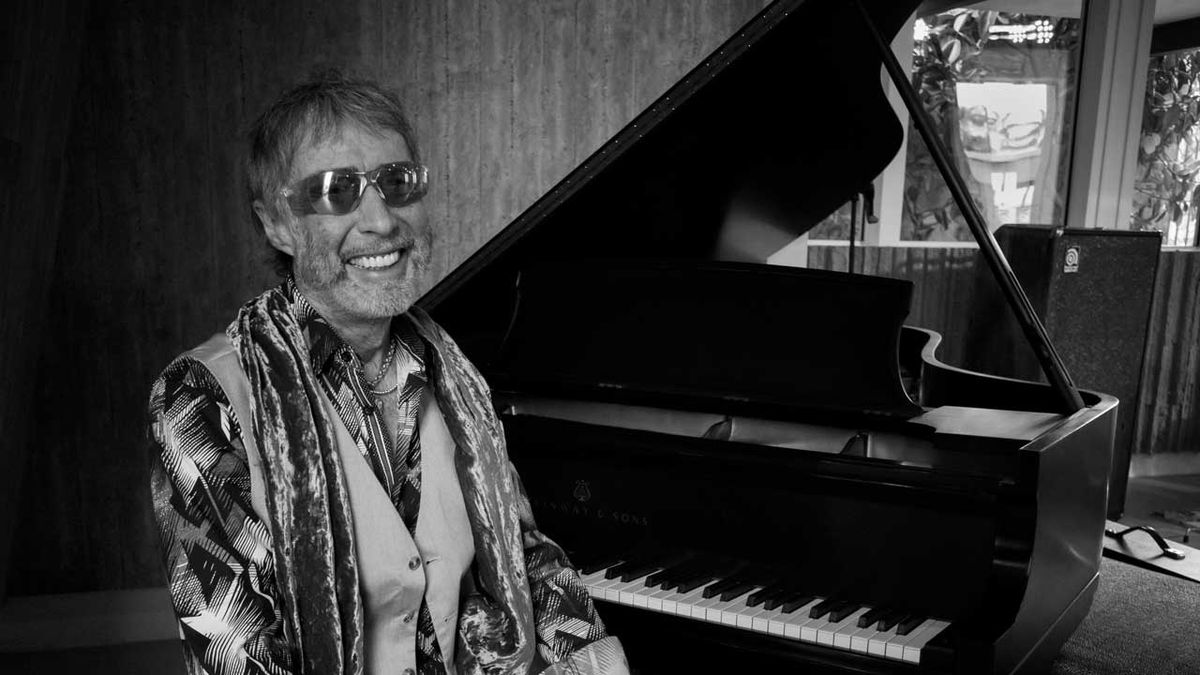 Paul Rodgers seated at a grand piano wearing sunglasses