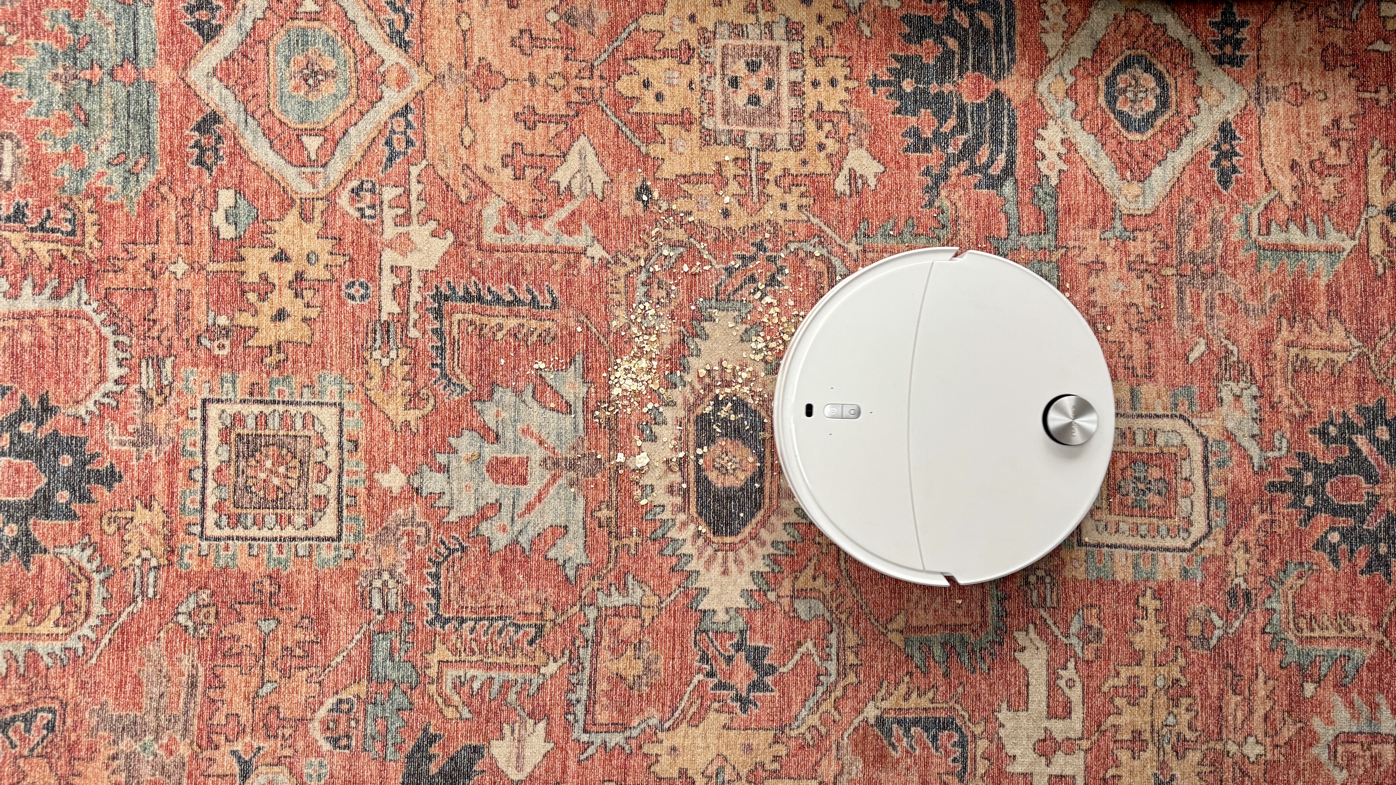 Roborock Qrevo Curv 2 Pro in the process of clearing oats and crumbs from a patterned carpet rug