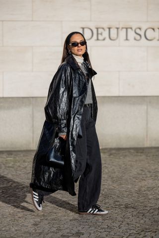 woman wearing sweater, leather trench coat, trousers, and adidas sambas sneakers