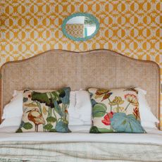 Yellow bedroom wallpaper with rattan headboard, turquoise mirror and floral throw cushions