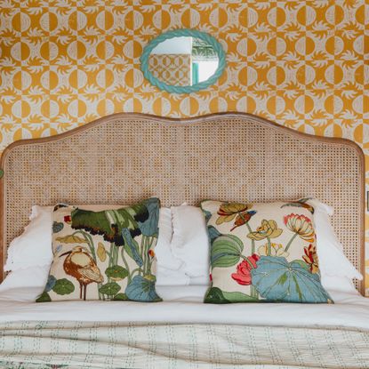 Yellow bedroom wallpaper with rattan headboard, turquoise mirror and floral throw cushions