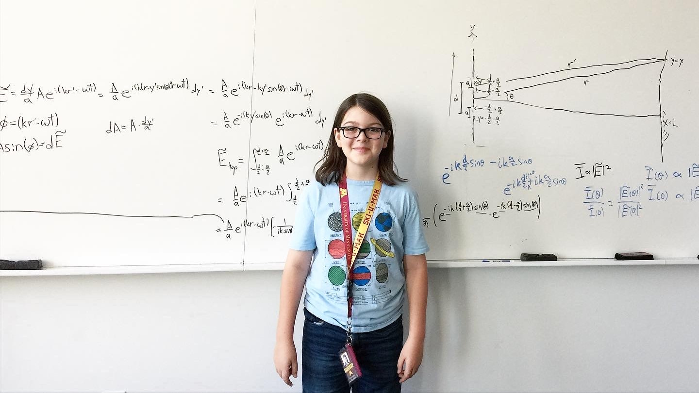 Elliott stands in front of a whiteboard filled with complex equations he solved.