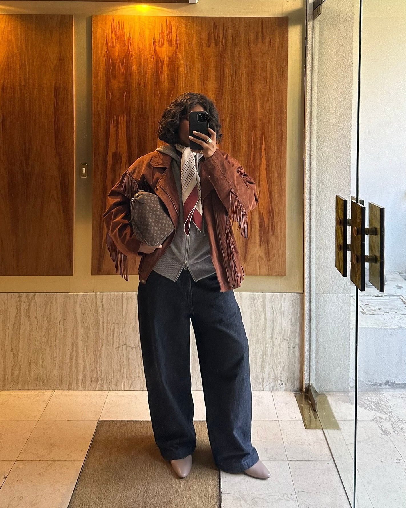 @frannfyne wearing a leather jacket, gray sweater, wide-leg jeans, and tan boots.