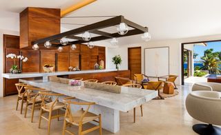 Villa One kitchen with granite dining table and overhead metal bulkhead with lights, wooden cabinets and cane chairs