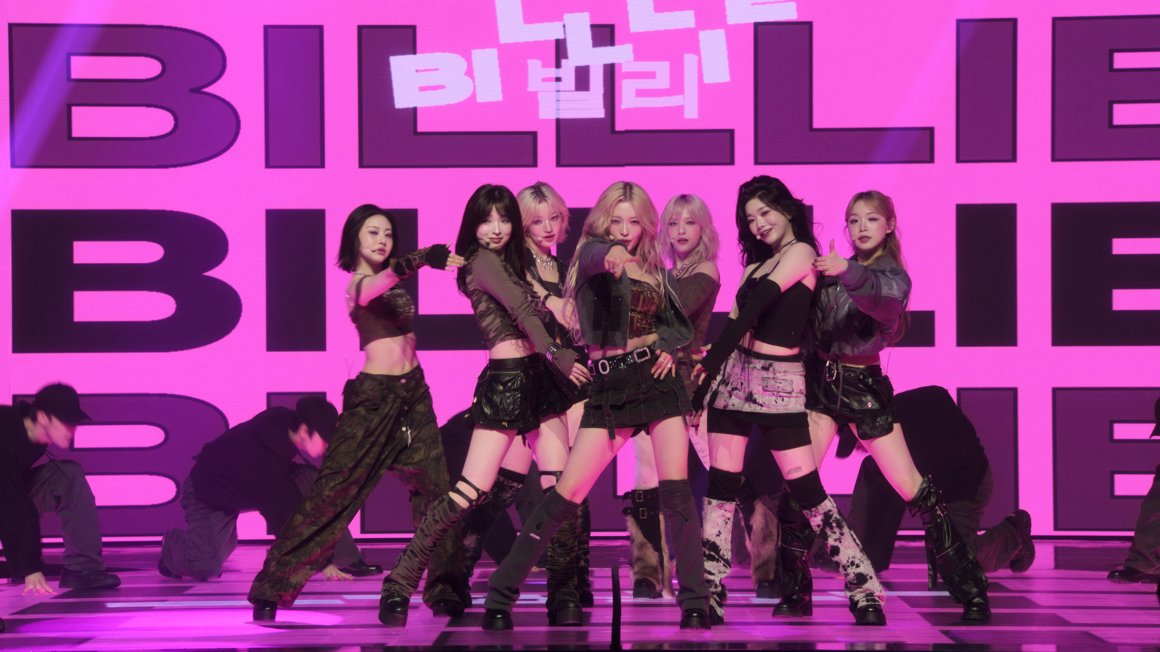 Seven women (from left: Sheon, Haruna, Siyoon, Haram, Moon Sua, Tsuki, and Suhyeon) perform in front of an LED screen repeating &amp;quot;Billlie&amp;quot; in English and Korean, on Apple TV+&#039;s &#039;KPOPPED.&#039;