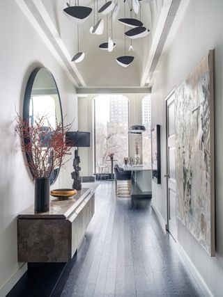A bright entryway with circular mirror, artwork, light fixture and console table