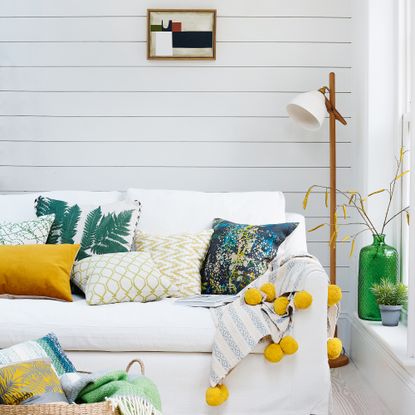 White linen sofa with yellow and green cushions in front of white panelled wall