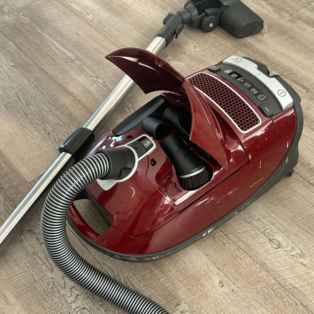 Miele Complete C3 Cat &amp; Dog PowerLine, one of the best vacuum cleaners for pet hair, on Megan's kitchen floor with the hidden compartment open to reveal the attachment brushes stored inside