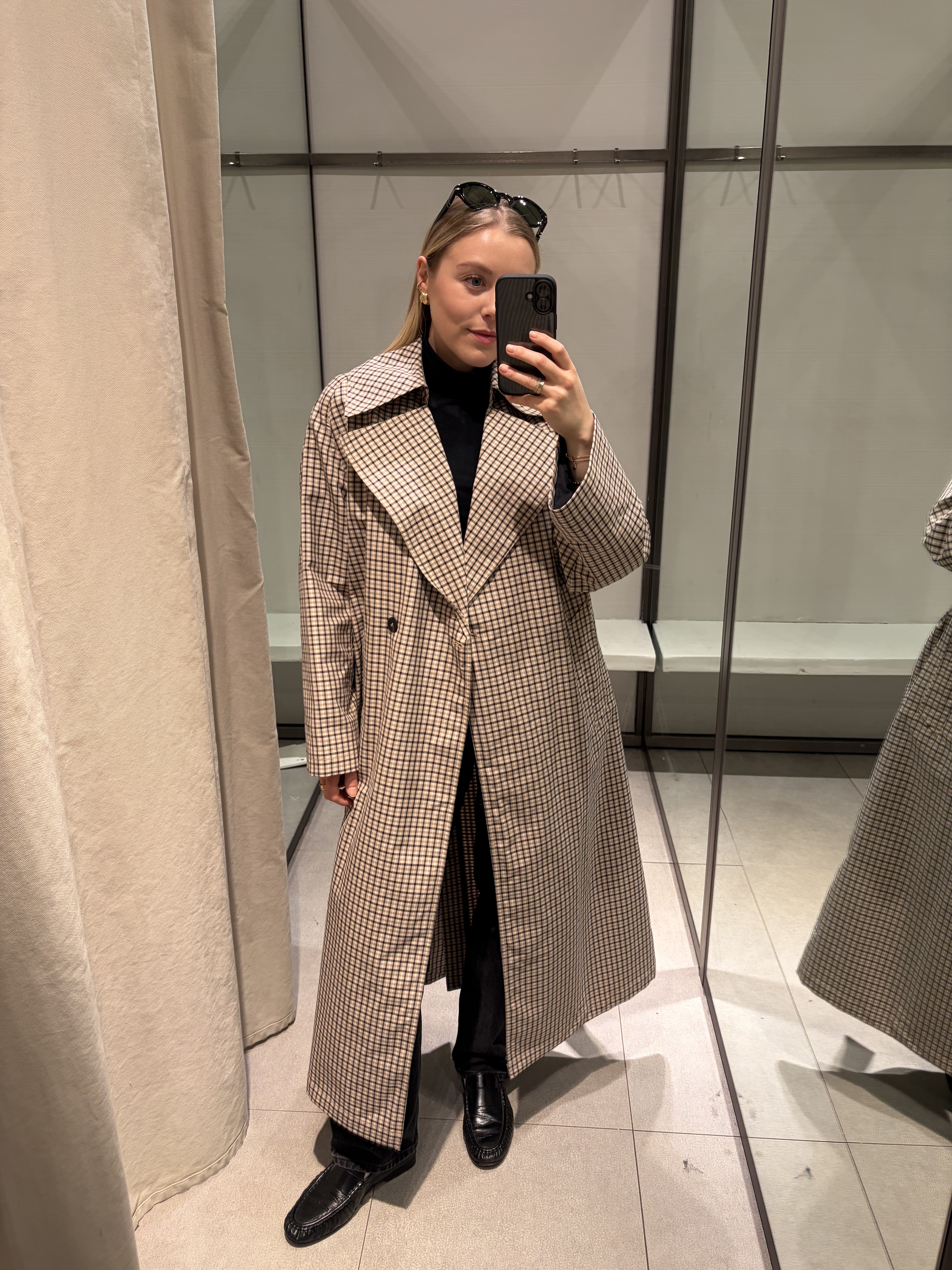 Woman wears check trench coat, black jeans and black loafers