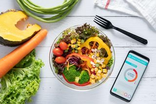 A bowls of salad next to a phone with a calorie counting app