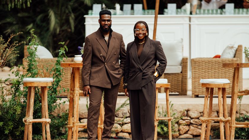 a man and a woman in brown standing in front of wicker stools in the sun