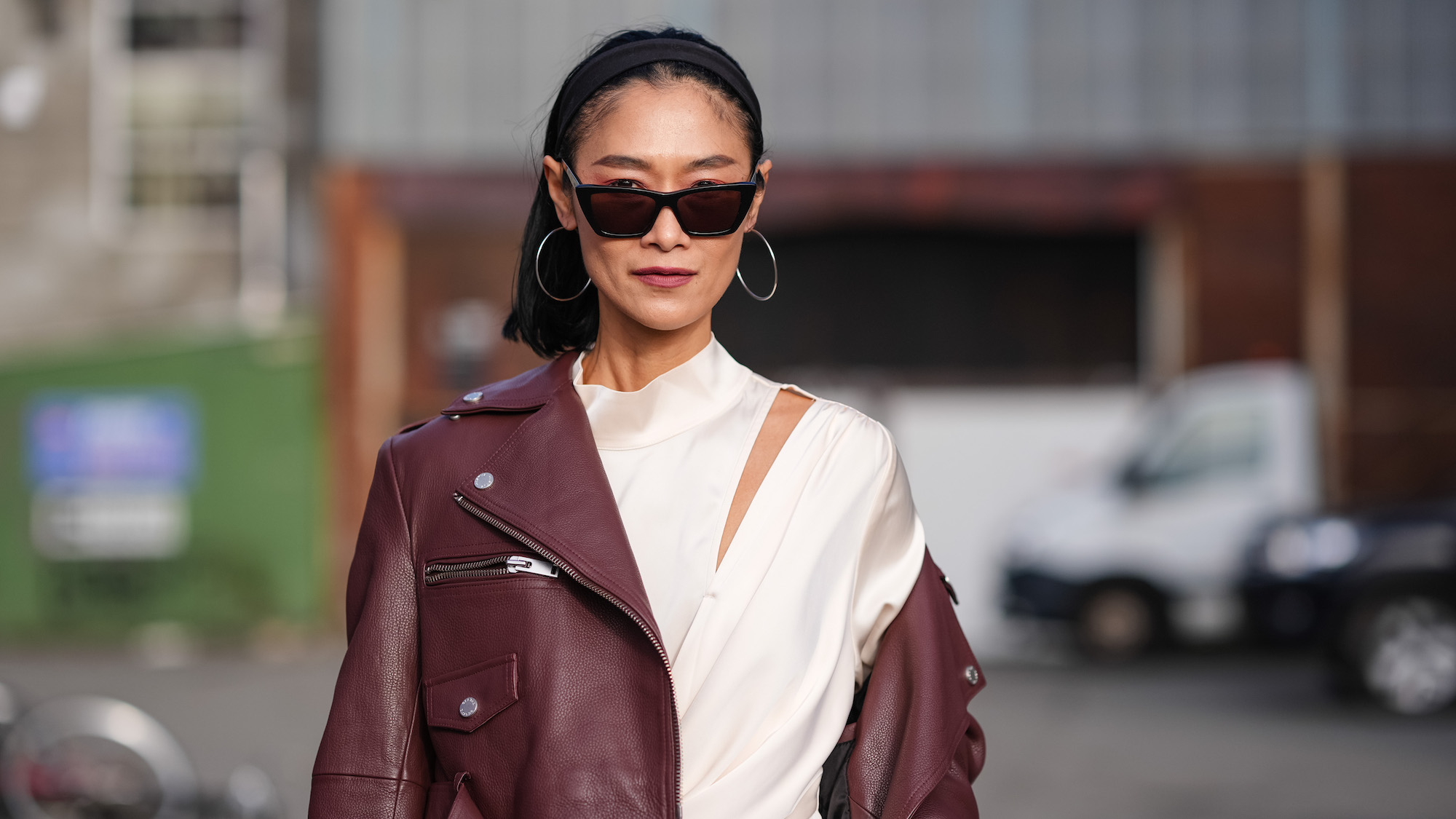 Pornwika Spiecker wears sunglasses, a burgundy leather biker jacket , a white gathered long dress and contoured makeup