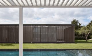 A pergola looks across a pool to the master bedroom, afforded privacy by the wooden screens