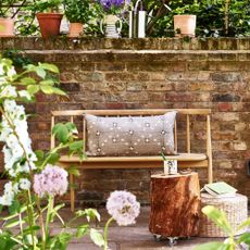 Wooden bench in front of garden wall with potted plants around a stump table 