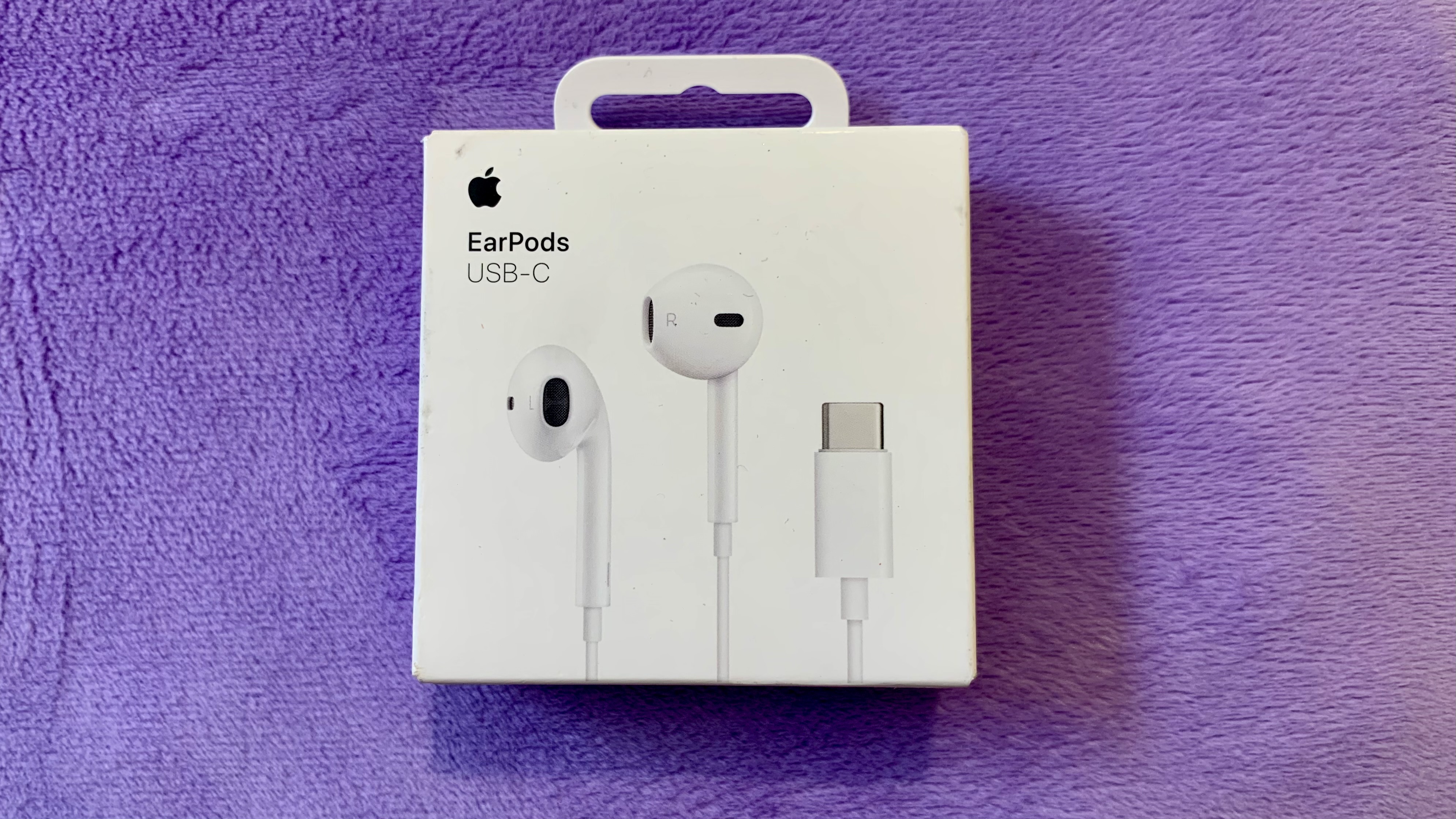 Apple USB-C EarPods dans leur emballage sur un coussin violet