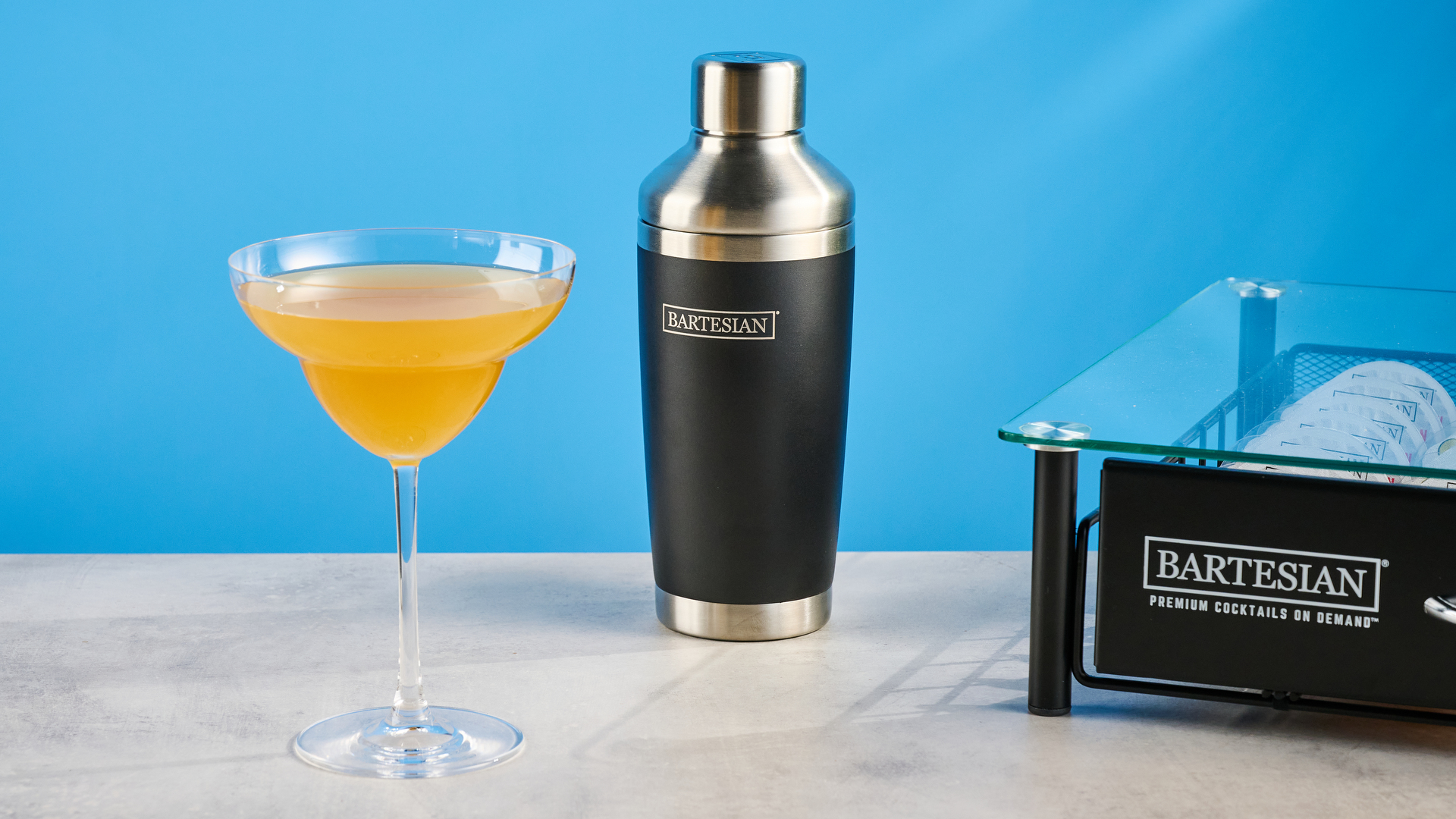 the bartesian premium cocktail machine photographed against a blue background showing its drink-making abilities and accessories and functionality with cocktail pods