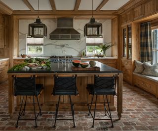 kitchen with wooden cabinets and island with black countertop and bar stools with brick floor