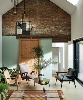 Modern farmhouse style living room with green wall, exposed brick, rug, sliding door, 3 armchairs,