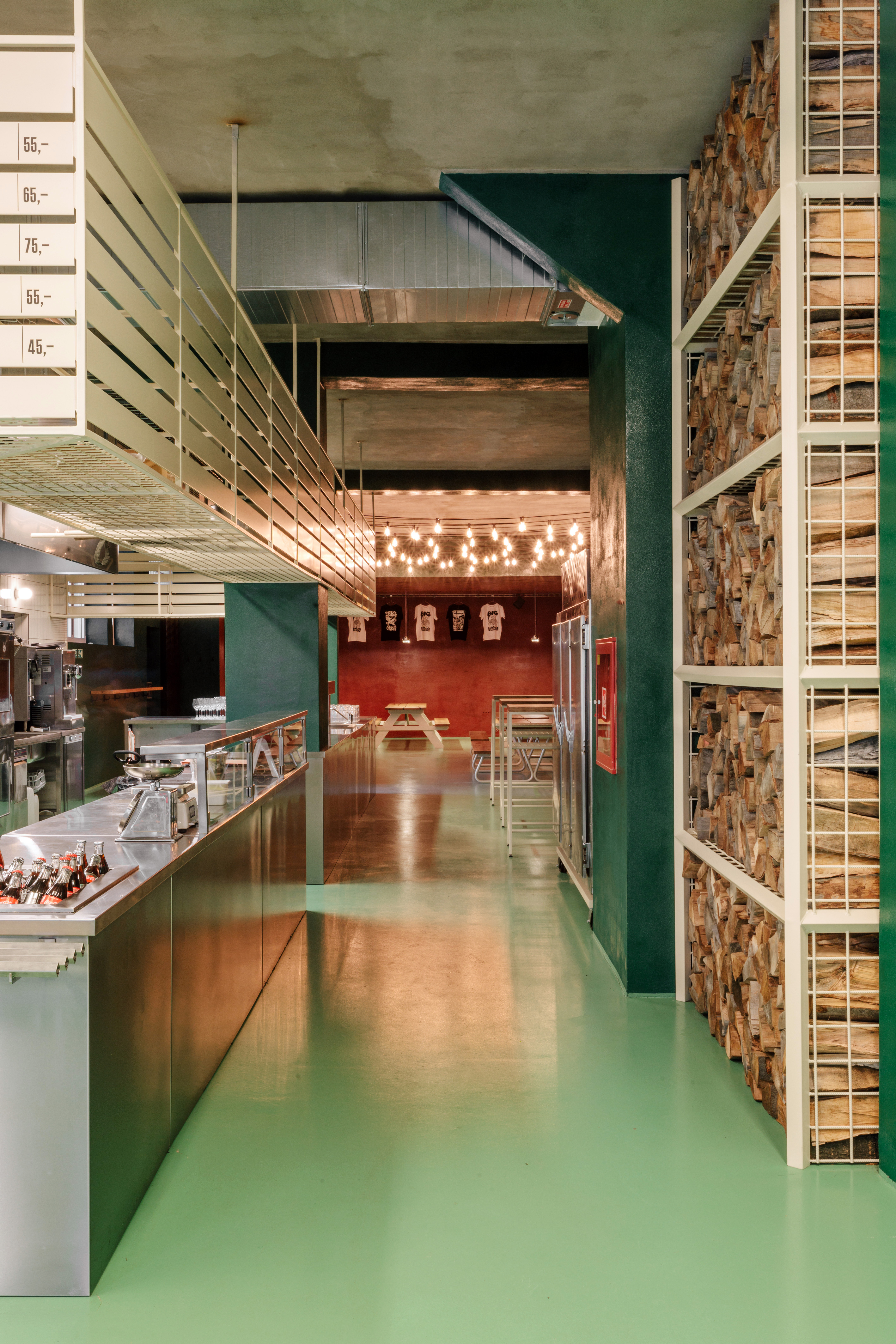 Interiors of a restaurant tucked inside an industrial site, with green painted walls and floors, a diner-inspired decor, and trails of fairy lights, along with wood and chrome details.