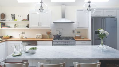 Modern white kitchen with marble island and an American-style fridge freezer in the background