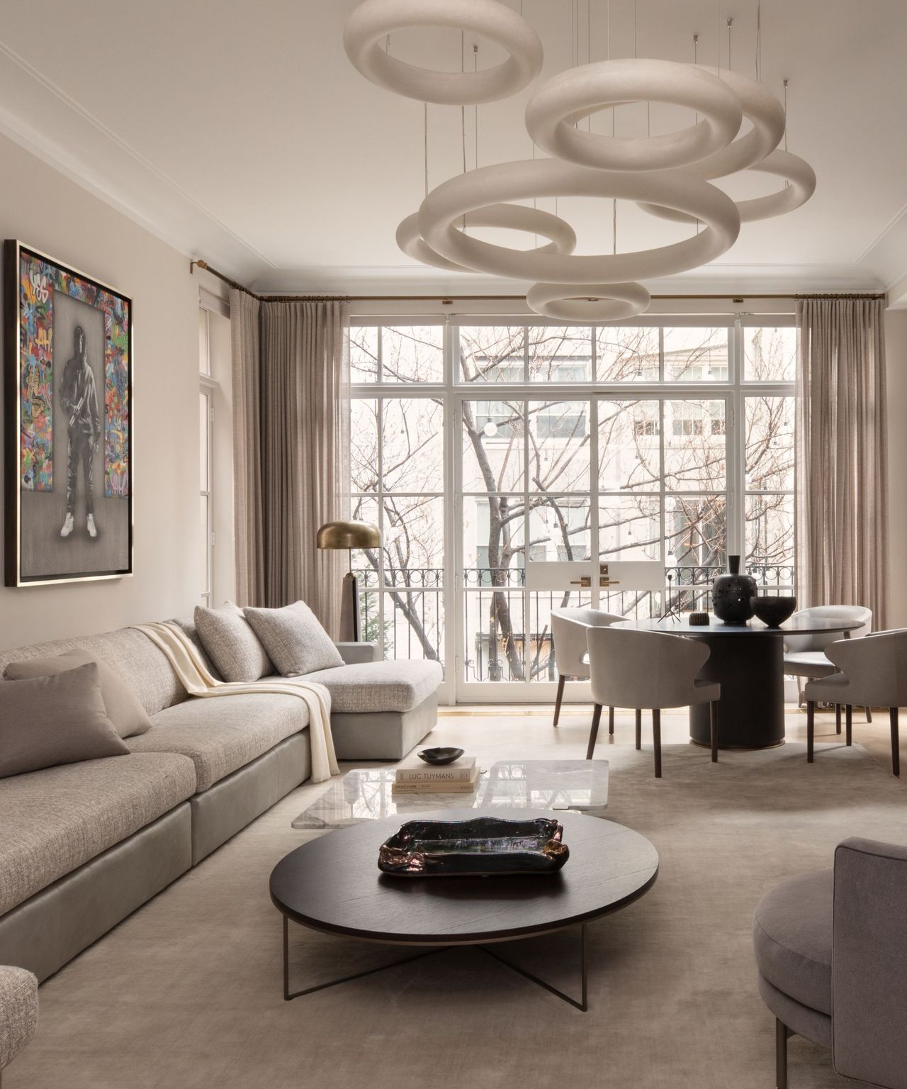 A neutral living room with sculptural lighting, a large sectional, and floor to ceiling windows