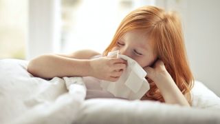 Young girl blowing nose in bed