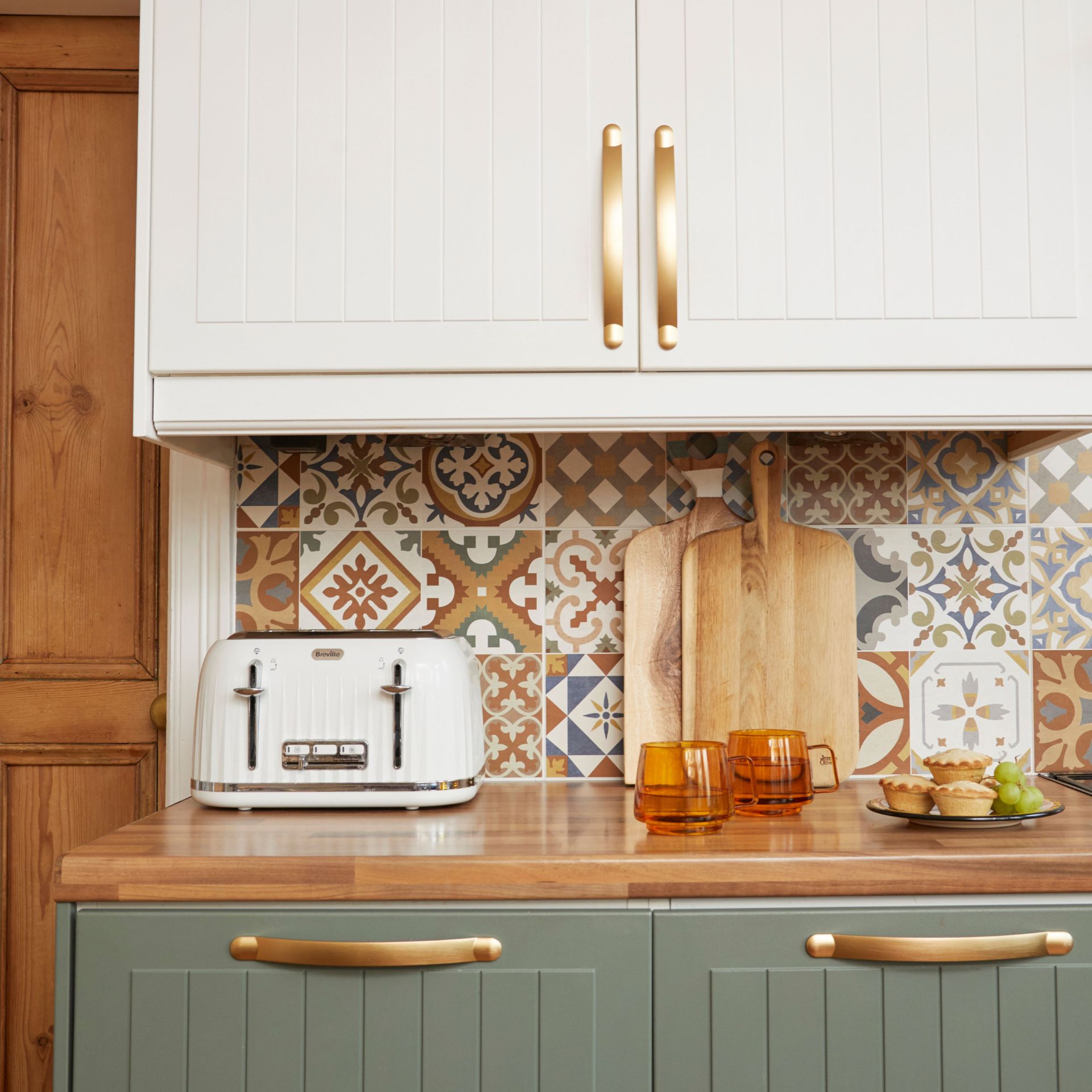 Kitchen with patterned backsplash, wooden worktop with green and white painted cabinetry, white toaster and accessories displayed on top