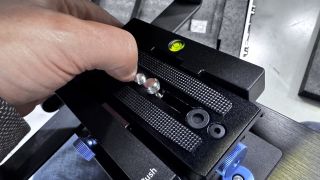 A hand touching the screws on the Neewer Teleprompter X14 III quick-release plate