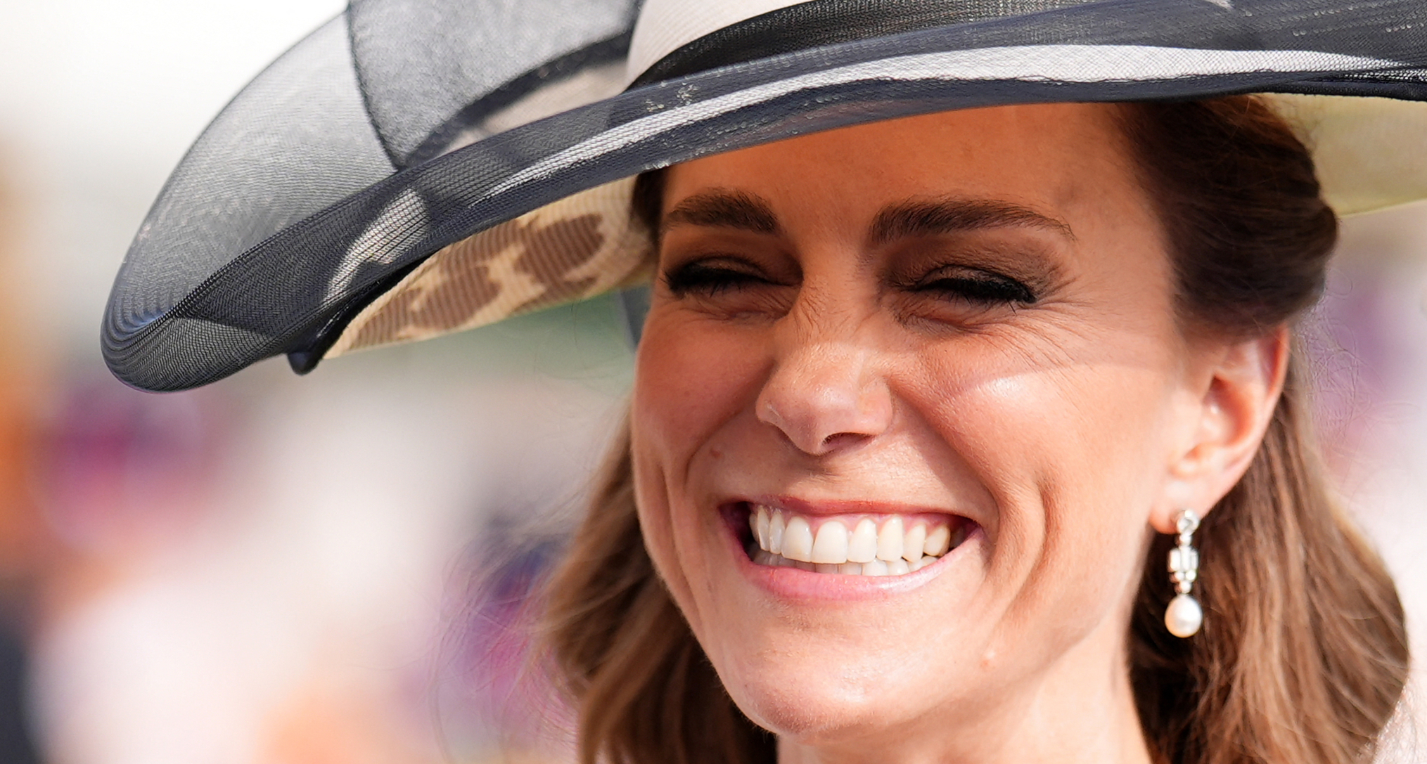 Princess Kate wearing a white hat with a black ribbon and smiling