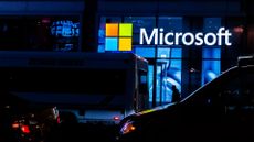Microsoft signage pictured in New York City at night with passing traffic and pedestrians.