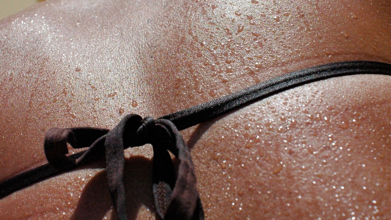 water droplets run down a woman&#039;s bare back and bikini while tanning