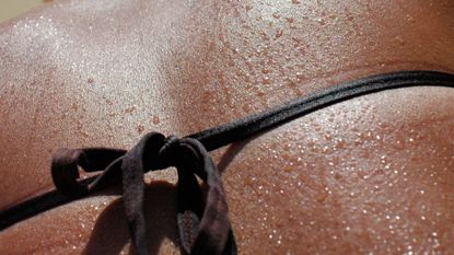 water droplets run down a woman's bare back and bikini while tanning