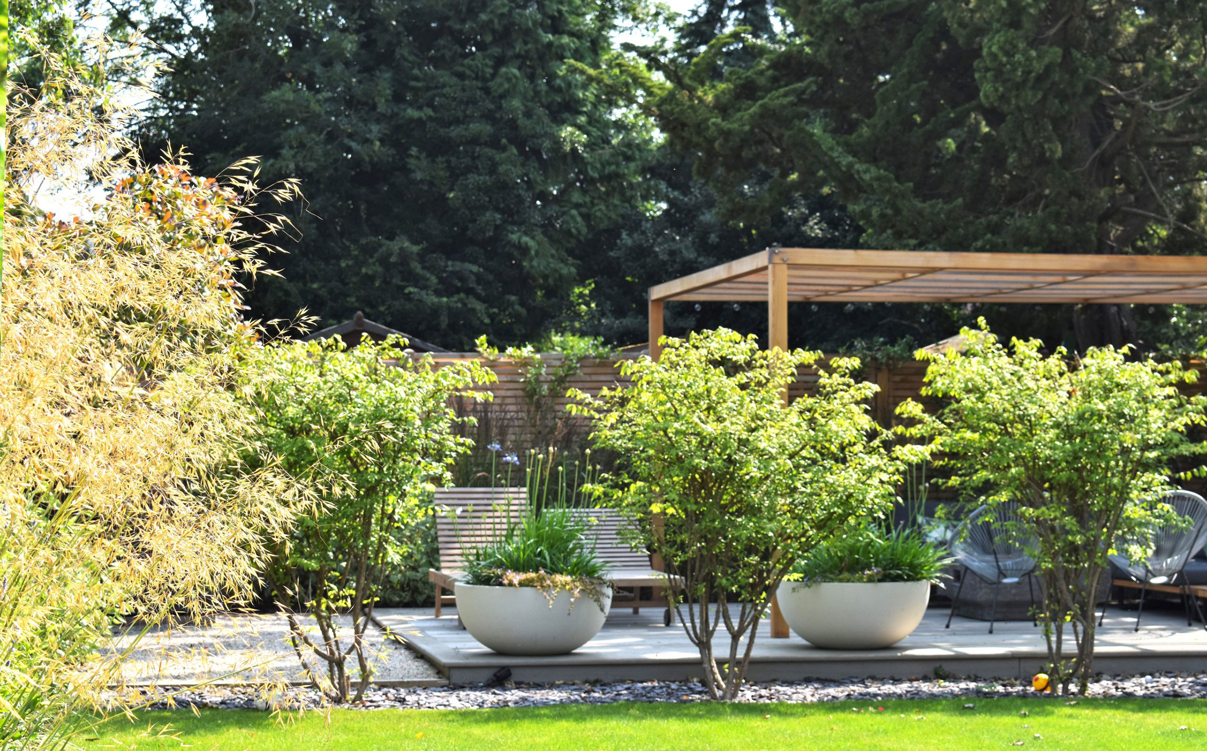 Curated yard space with neat garden, surrounding planting, decking space and slat patio furniture