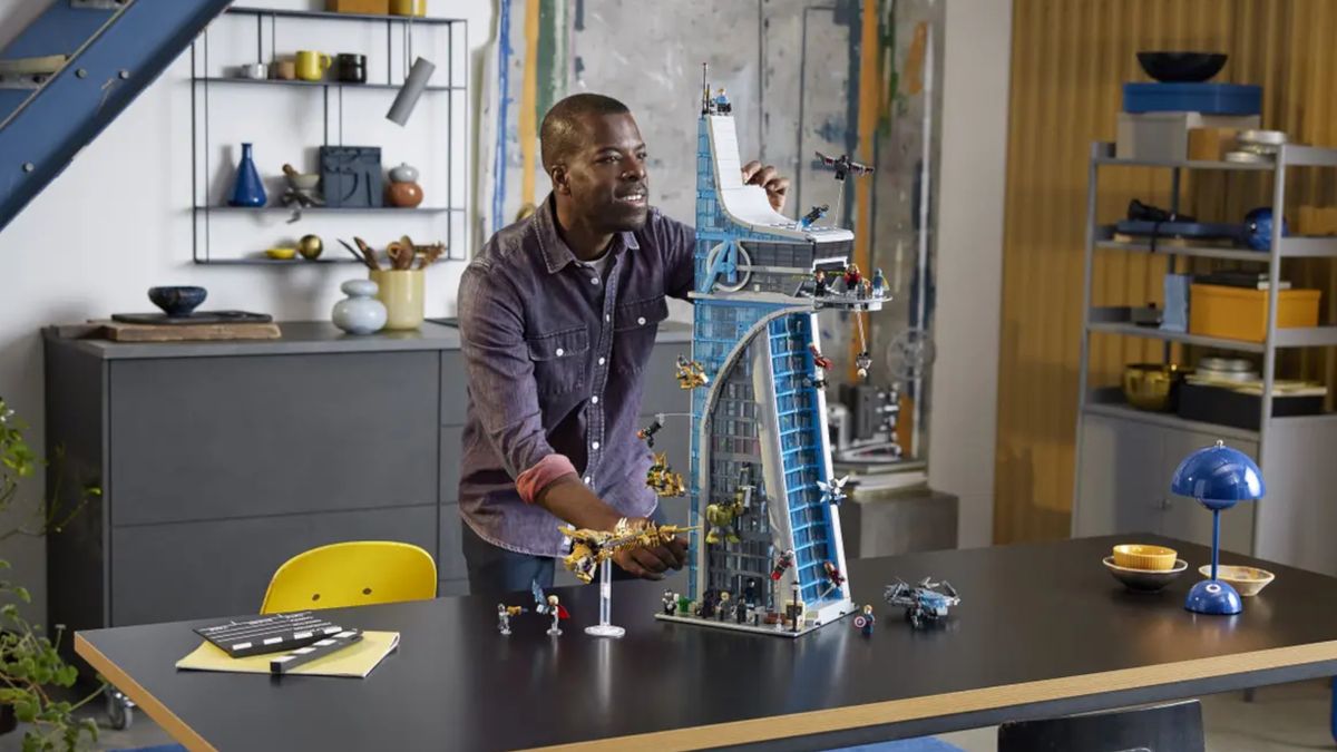 A man builds Lego Avengers Tower on a wooden table