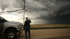 A scientist stands next to a truck strapped with monitoring equipment as he observes a tornado
