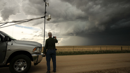 A scientist stands next to a truck strapped with monitoring equipment as he observes a tornado