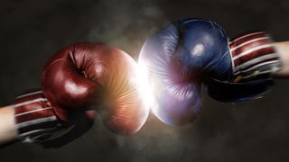 A close-up of a two boxing gloves hitting each other, one is red and the other blue to represent Republicans and Democrats, respectively.