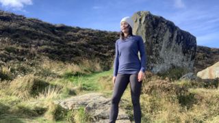 Woman hiking in blue top with large rock behind her