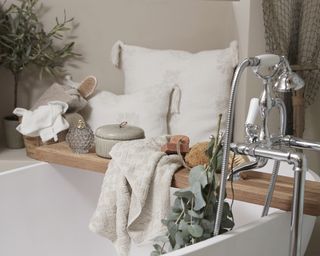 wooden bath caddy on a bath with decorative candles, jars and flowers
