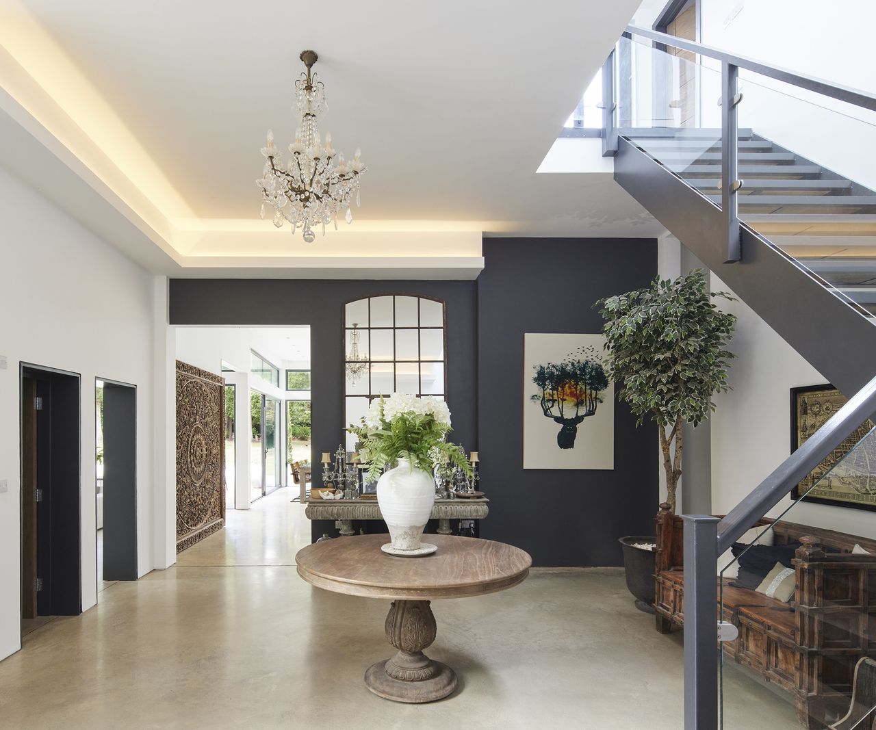 a large hallway with central circular table with vase and a hanging chandelier