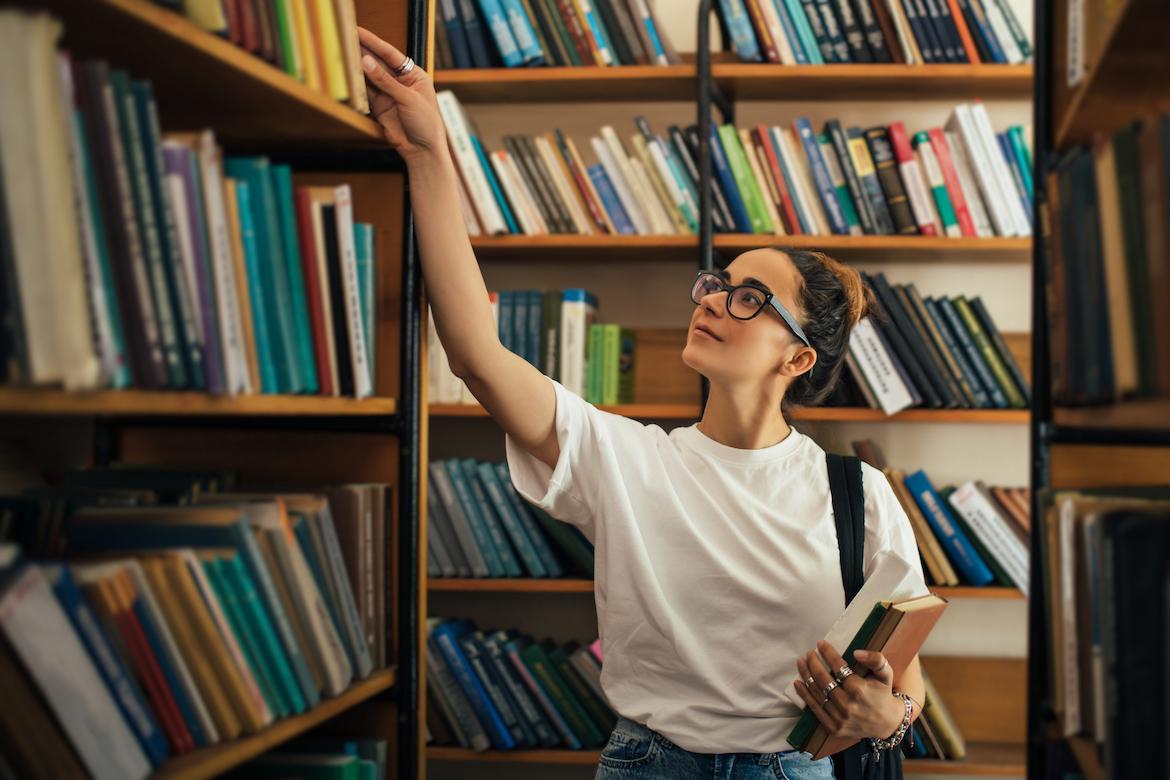 A student looking through a library holding a few books in their arm