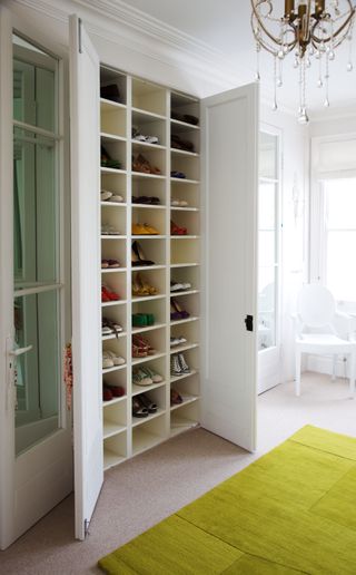 Shoe closet with cubbies and white doors in room with neutral carpet, green rug and chandelier