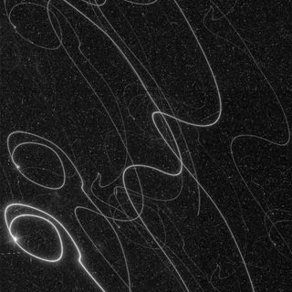 long swirly lines of white light are scribbled across the image against a background of stars.