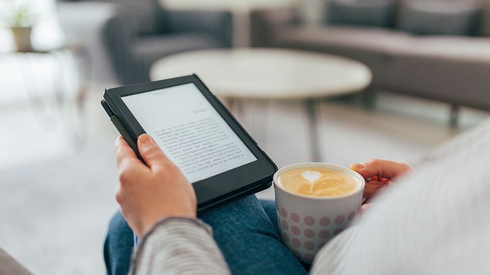 A man reading on a Kindle while drinking a coffee