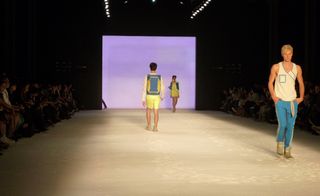 Three models on a runway, displaying clothing in yellow and blue