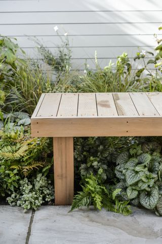 a garden bench next to a light painted fence in amongst foliage