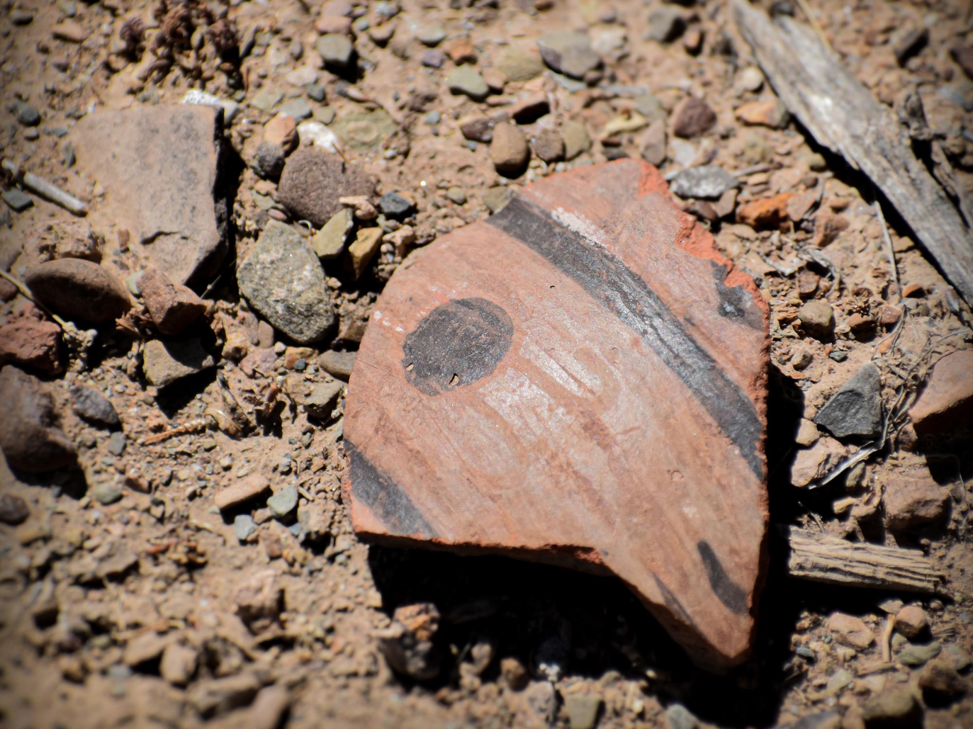 A shattered piece of terracotta-colored pottery sits on dirt.