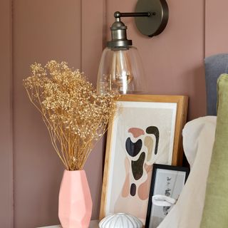 Close up of vase and artwork on bedside table below glass wall light